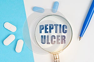 On a white and blue surface are pills, a pen and a magnifying glass with the inscription - Peptic ulcer