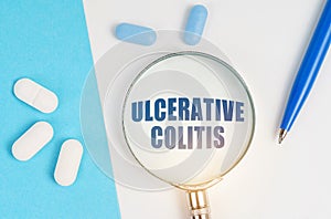 On a white and blue surface are pills, a pen and a magnifying glass with the inscription - ULCERATIVE COLITIS