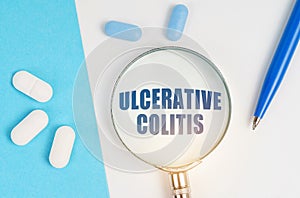 On a white and blue surface are pills, a pen and a magnifying glass with the inscription - ULCERATIVE COLITIS photo