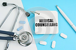 On a white and blue surface are pills, a stethoscope, a pen and a notepad with the inscription - Medical Counselling