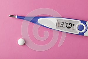 White-blue thermometer with a high temperature of 37.0 degrees Celsius in hand with medical pills