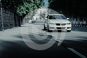 White BMW 3 Series F30 car standing on empty asphalt road at summer daytime