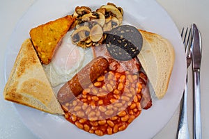 White board with full English breakfast with bacon, fried egg, beans, tomato, roasted sausage, black pudding, scons, hash browns