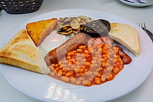 White board with full English breakfast with bacon, fried egg, beans, tomato, roasted sausage, black pudding, scons, hash browns