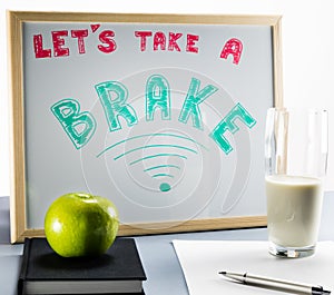 A white board titled `Let`s take a brake` with red and green letters, cup of milk and a green apple.