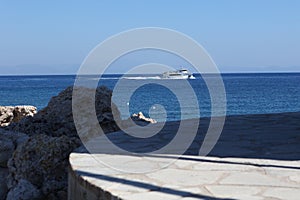 white boat on an azure blue sea. Stones in the foreground. Sunny sky