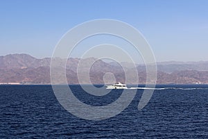 White boat in the red sea in Eilat against the background of the pink mountains of Jordan.