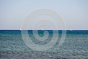 3 White boats sailing in the open blue aegean sea in