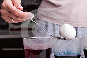 A white boiled egg on an iron spoon in women`s hands before dipping into a transparent glass with dilute concentrated food