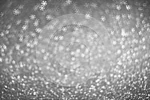 White bokeh lights in the form of snowflakes on a gray silver background. Winter background