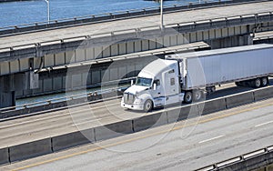 White bonnet big rig semi truck tractor transporting cargo in refrigerated semi trailer running on the multilevel overpass road