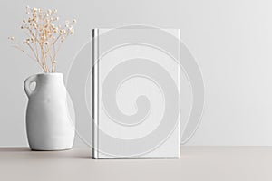 White book mockup with gypsophila in a vase on a beige table