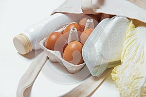 White bottle, chinese cabbage, quark, eggs in tote bag on white background side look