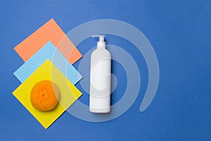 White bottle with cleaning agent, scrubber and napkins on blue colored paper background with copy space top view