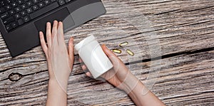 White bottle with omega vitamin pills in the hand and laptop on wooden background