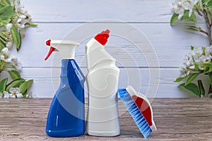 White bottle, spray, blue cleaning brush, cleaning set on spring background, pastel wooden planks and spring blossoms