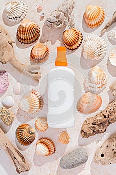 White bottle of sunscreen on background of seashells in hard light, top view. Sun protection lotion flat lay, creative image