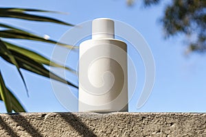 A white bottle with a white cap sits on a ledge in the sun