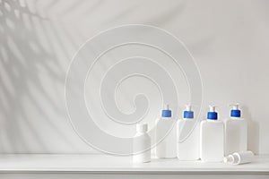 White bottles with blue dispenser with shampoo, conditioner, cream and liquid soap stand on a shelf in the bathroom. Place for