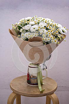 White bouquet of daisies and chrysanthemums wrapped in newsprint in a vase, cropped