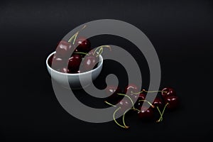 White bowl of black cherries isolated on black background