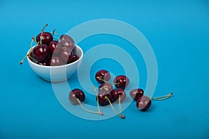 White bowl of black cherries isolated on blue background