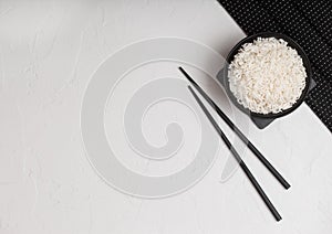 White bowl with boiled organic basmati jasmine rice with black chopsticks on bamboo place mat on white background. Space for text