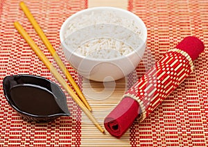 White bowl with boiled organic basmati jasmine rice with wooden chopsticks and sweet soy sauce on bamboo placemat background