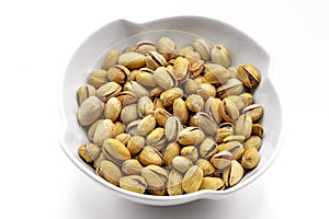 A white bowl with a bunch of salted and roasted pistachio seeds on a white background. Perfect shot for vegan diet