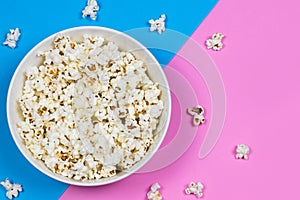 White bowl filled with popcorn on a blue and pink background