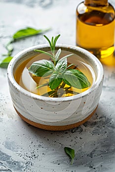 A white bowl filled with rosemary and basil leaves next to a bottle of oil photo