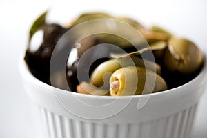 White bowl with fresh black and green olives, garlic, bay leaves on grey background. Copy space