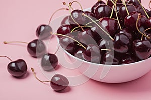 White bowl of fresh red cherries on a pink background. close-up