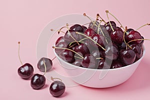 White bowl of fresh red cherries on a pink background. Copy space. close-up