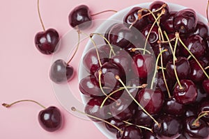White bowl of fresh red cherries on a pink background. Top view. close-up
