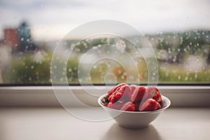 White bowl of organic fresh strawberries on a windowsill with raindrops. Fresh strawberries in the ceramic bawl photo