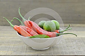 White bowl with red hot chili peppers and lemon on wooden background