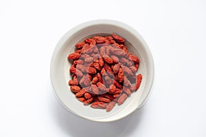 White bowl of red dried goji berries isolated on white background