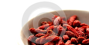 White bowl of red dried goji berries isolated on white background