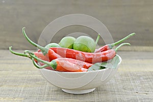 White bowl with red hot chili peppers and lemon on wooden background