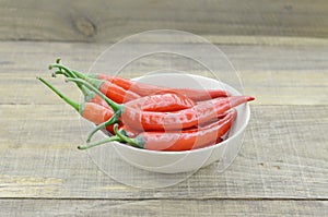 White bowl with red hot chili peppers on wooden background