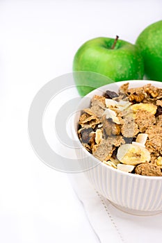 White bowl with rye flakes muesli on white towel with green apples, copyspace for text, white background