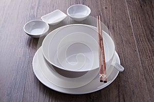 White bowl, spoon, sauce bowl and chopsticks on wood table