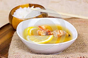 White bowl with traditional light spicy thai cuisine tom yam soup with shrimps, seafood and lemon on wooden board background.