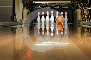 White bowling pins and an orange ball on a bowling alley. reflection