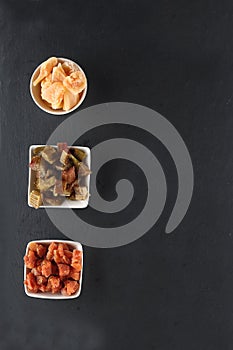 White bowls of candied rheum, pumpkins and cantaloup rock melon isolated on black background flat lay