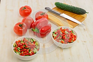 White bowls with fresh salad of green cucumbers, red tomatoes and bell peppers on light wooden surface. Vegetables. Lowcalorie photo