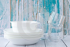 White bowls, glasses and plates on the table. Stack of clean dishes on a blue wooden background