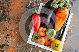 White box with vegetables on a rusty background. Aubergines, bell pepper, tonatoes.