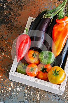 White box with vegetables on a rusty background. Aubergines, bell pepper, tonatoes.